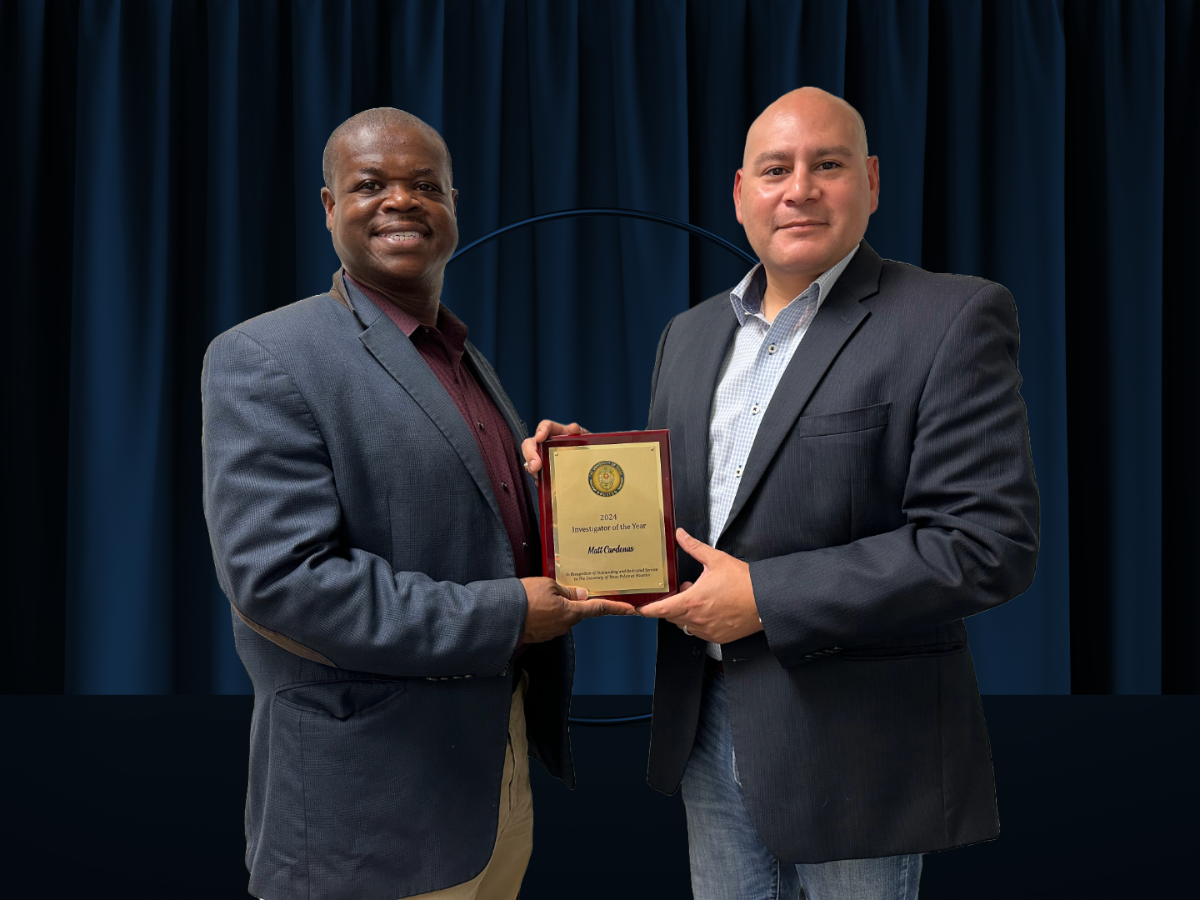 Two people in business attire stand before a dark blue curtain, smiling while jointly holding a wooden-framed award plaque.